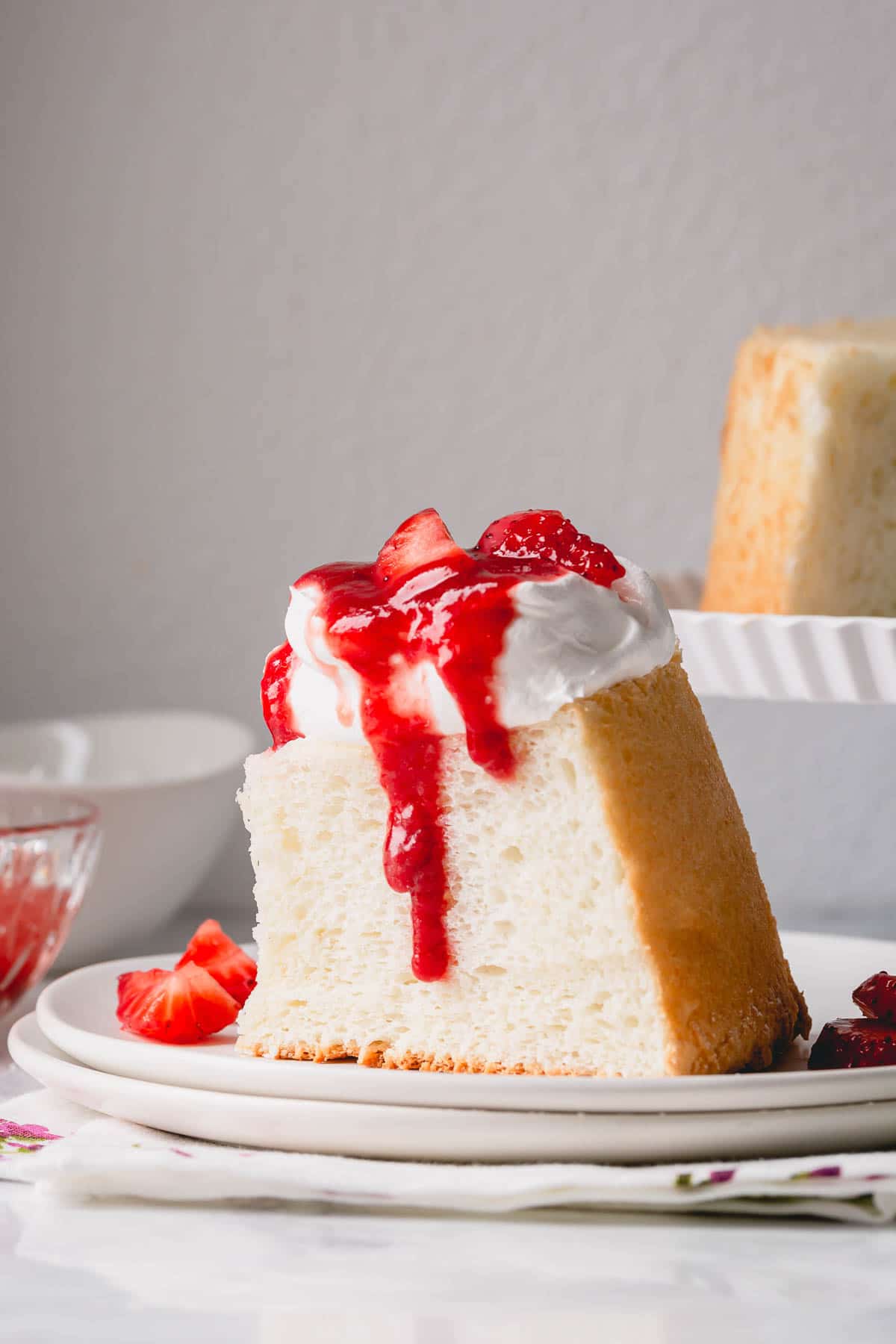 A slice of angel food cake topped with whipped cream and strawberry sauce.