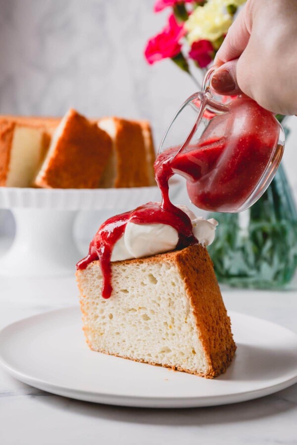A slice of angel food cake topped with whipped cream and strawberry sauce.