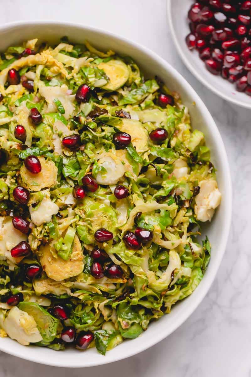 A bowl of shaved Brussels sprouts topped with pomegranate arils.