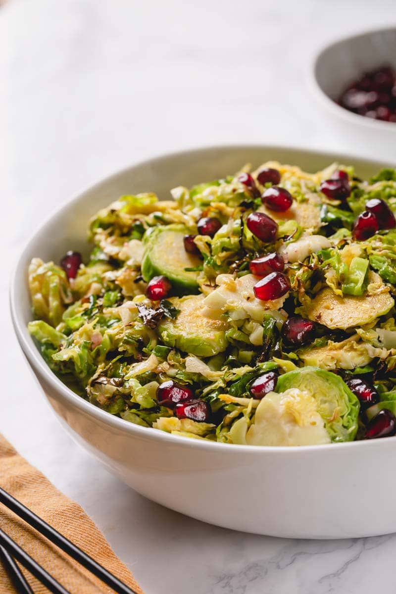 A bowl of shaved Brussels sprouts salad topped with pomegranate arils.