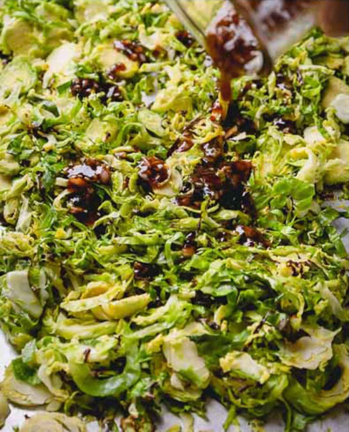 Pomegranate vinaigrette is being poured over roasted brussels sprouts.