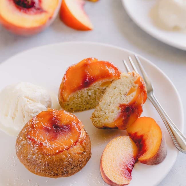 Peach upside down mini cakes on a white serving plate with vanilla ice cream and sliced peaches.
