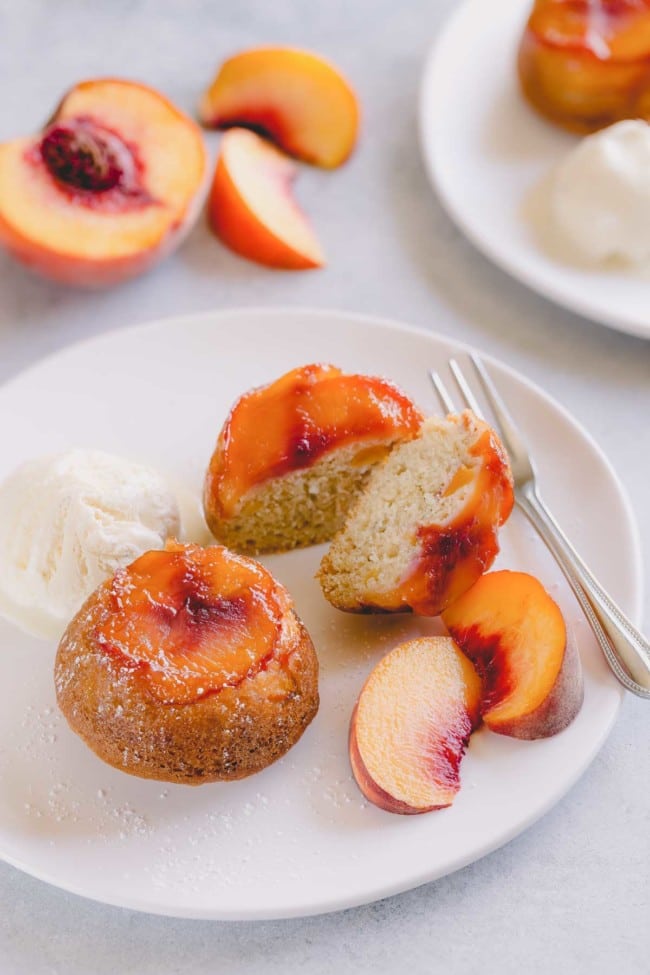 Peach upside down mini cakes on a white serving plate with vanilla ice cream and sliced peaches.