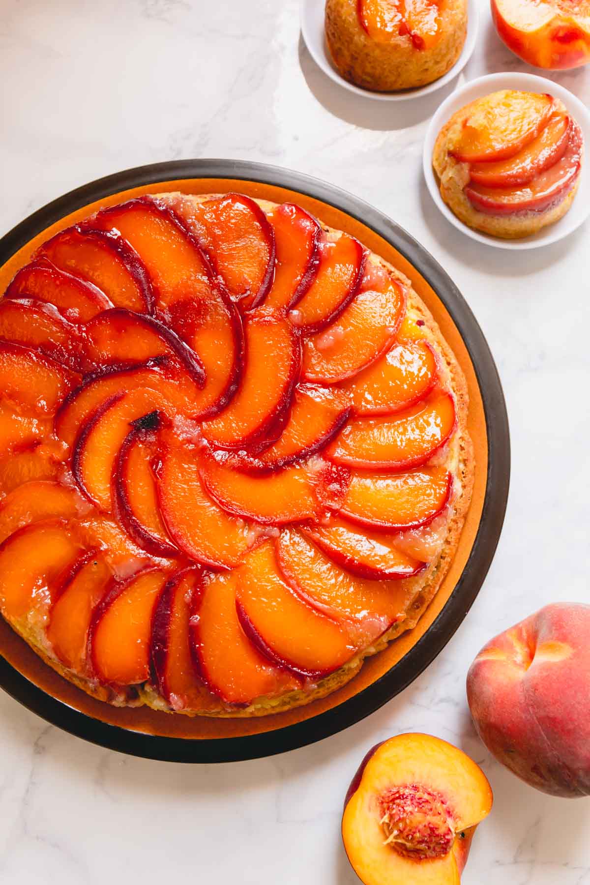 A round peach upside down cake on a larger serving plate.