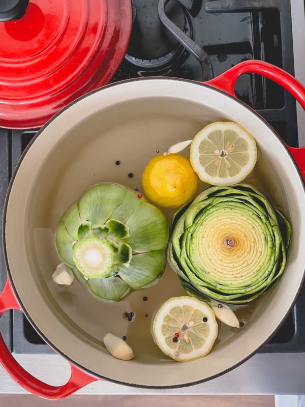 Artichokes boiled in a pot with lemon slices and aromatics.