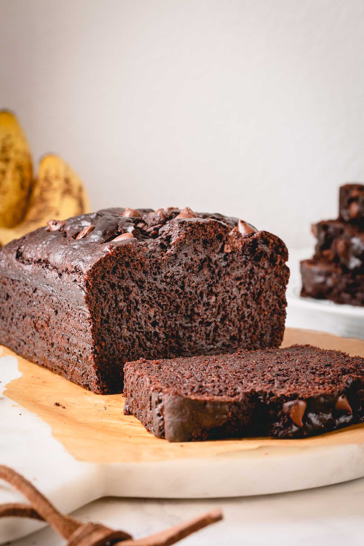 loaf of chocolate banana bread with one slice cut on cutting board
