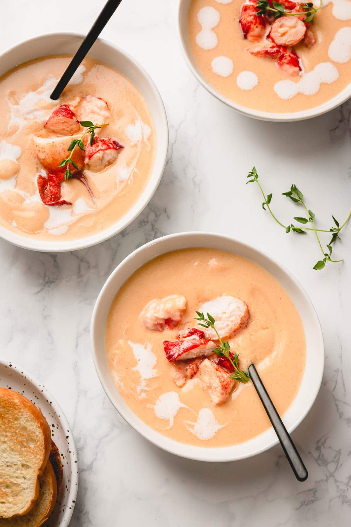 3 bowls of creamy lobster bisque garnished with chunks of lobster meat and fresh thyme.