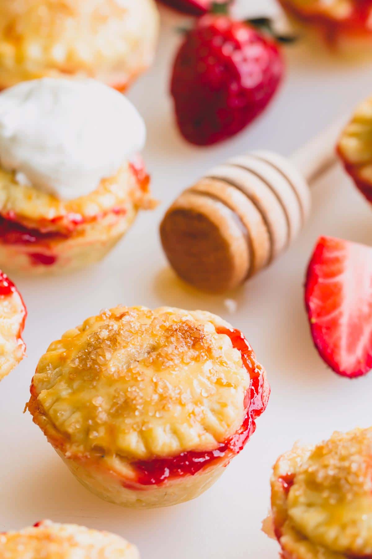 Mini strawberry pies on a white surface with a honey dipper.