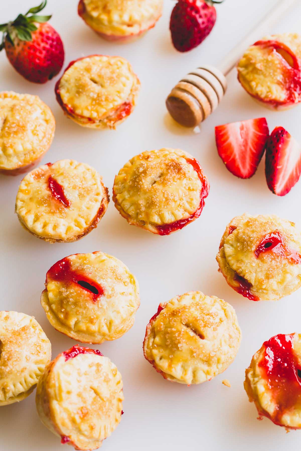 Mini strawberry pies on a white surface with decorative strawberries on the side.