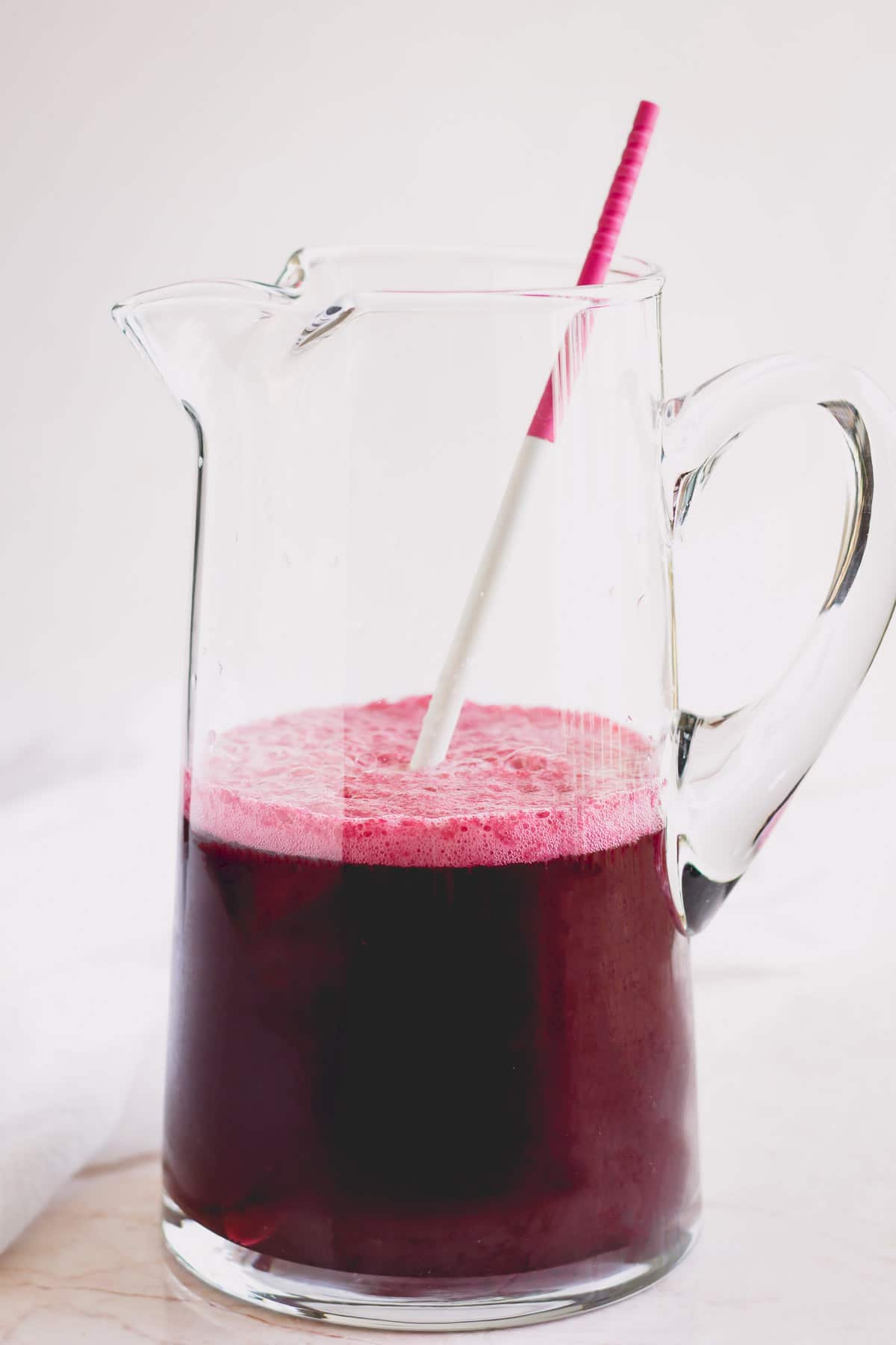 Large jug of blueberry lemonade with a long pink and white stirrer in it.