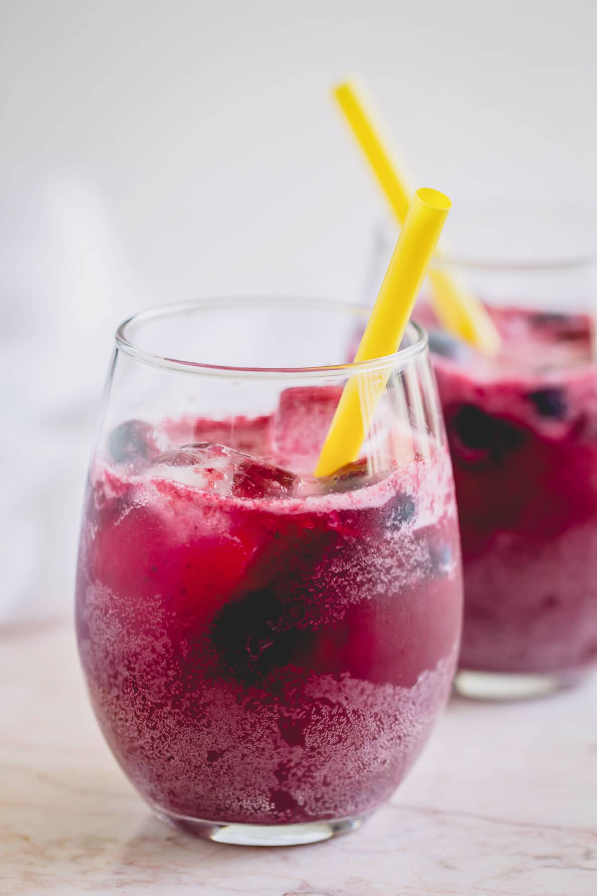 Glass of sparkling blueberry lemonade with a yellow straw.