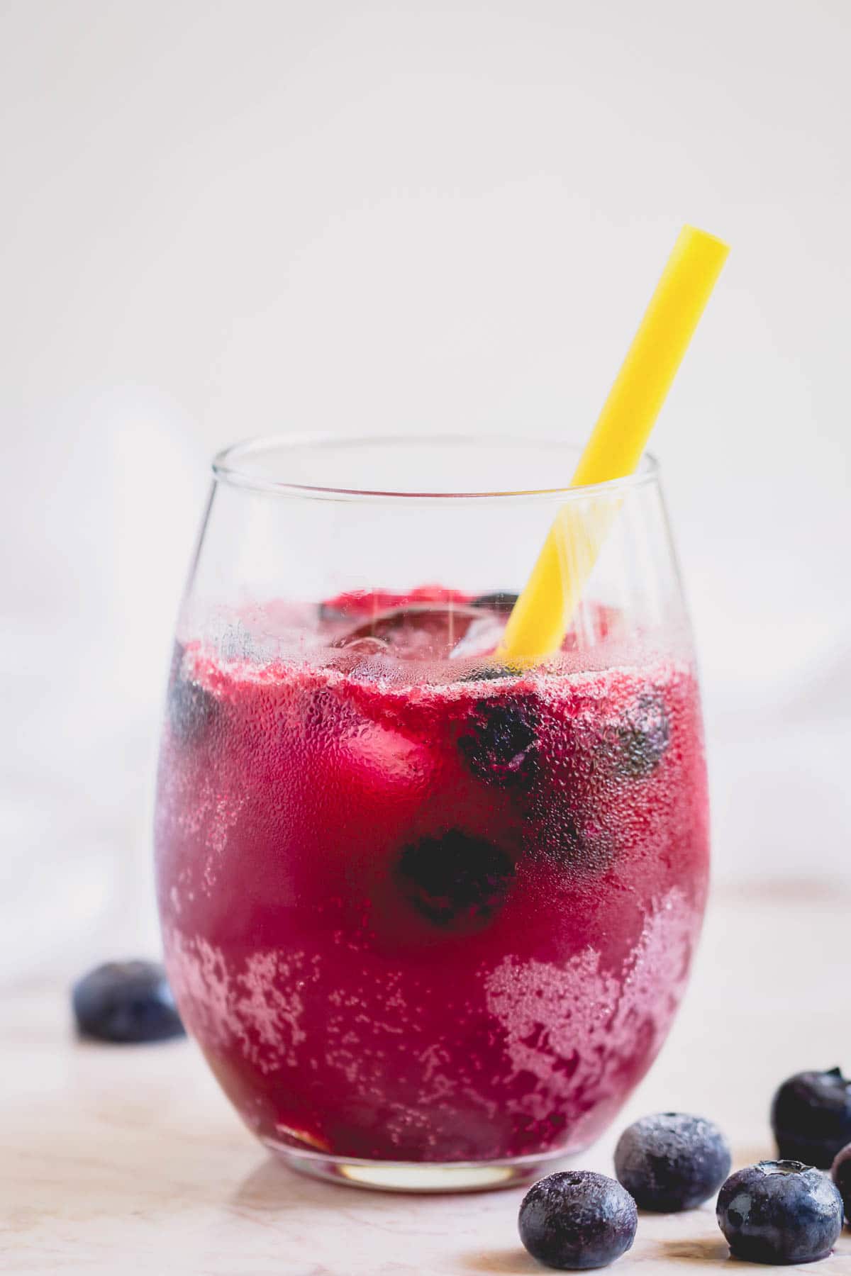A glass of sparkling blueberry lemonade with a yellow straw.