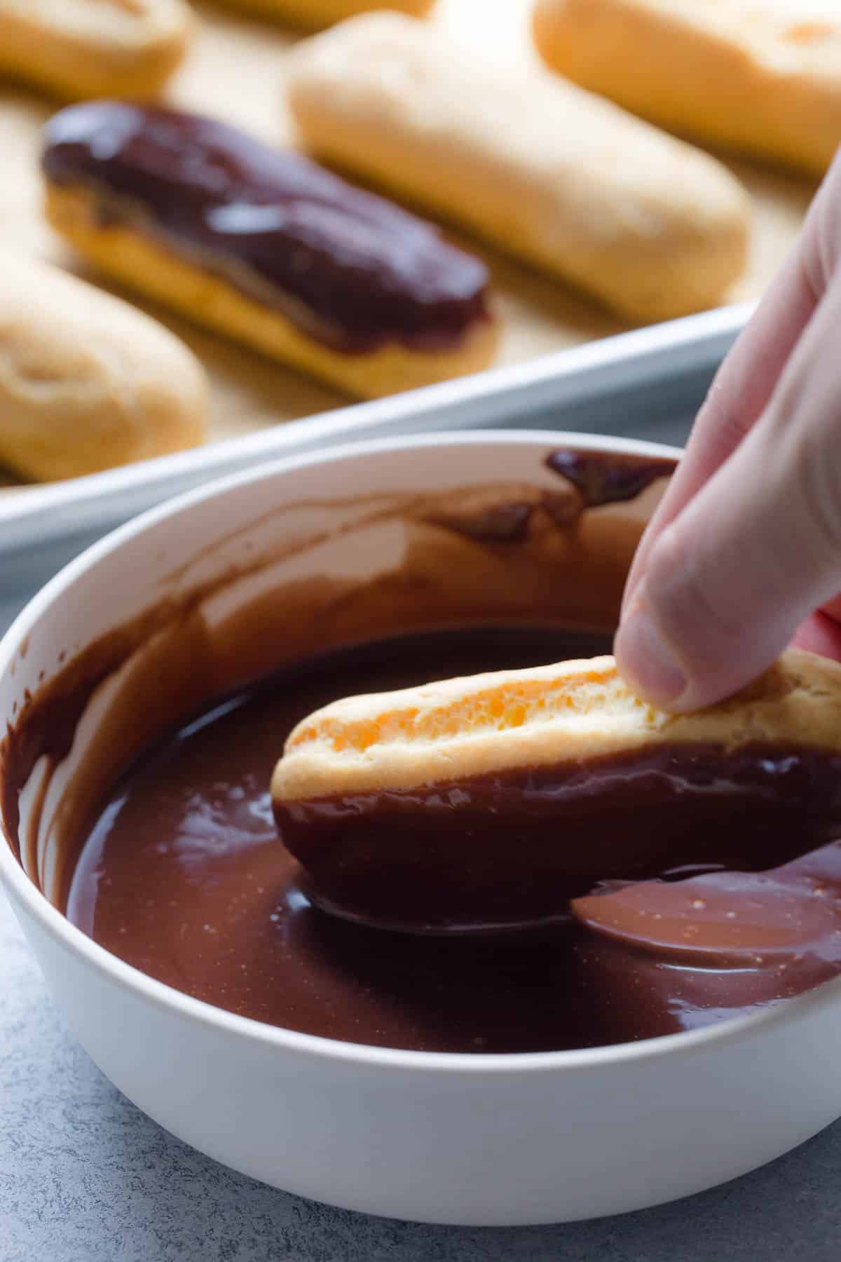Filled eclairs is being dipped in a bowl of chocolate ganache.