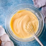 Smooth pastry cream in a glass bowl with a whisk.