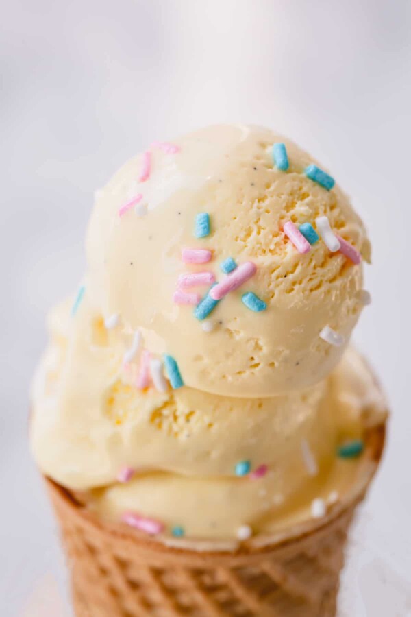 three vanilla ice cream scoops with sprinkles stacked on wafer cone.