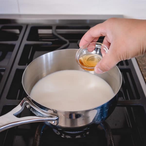 A saucepan with milk and vanilla extract on a burner.