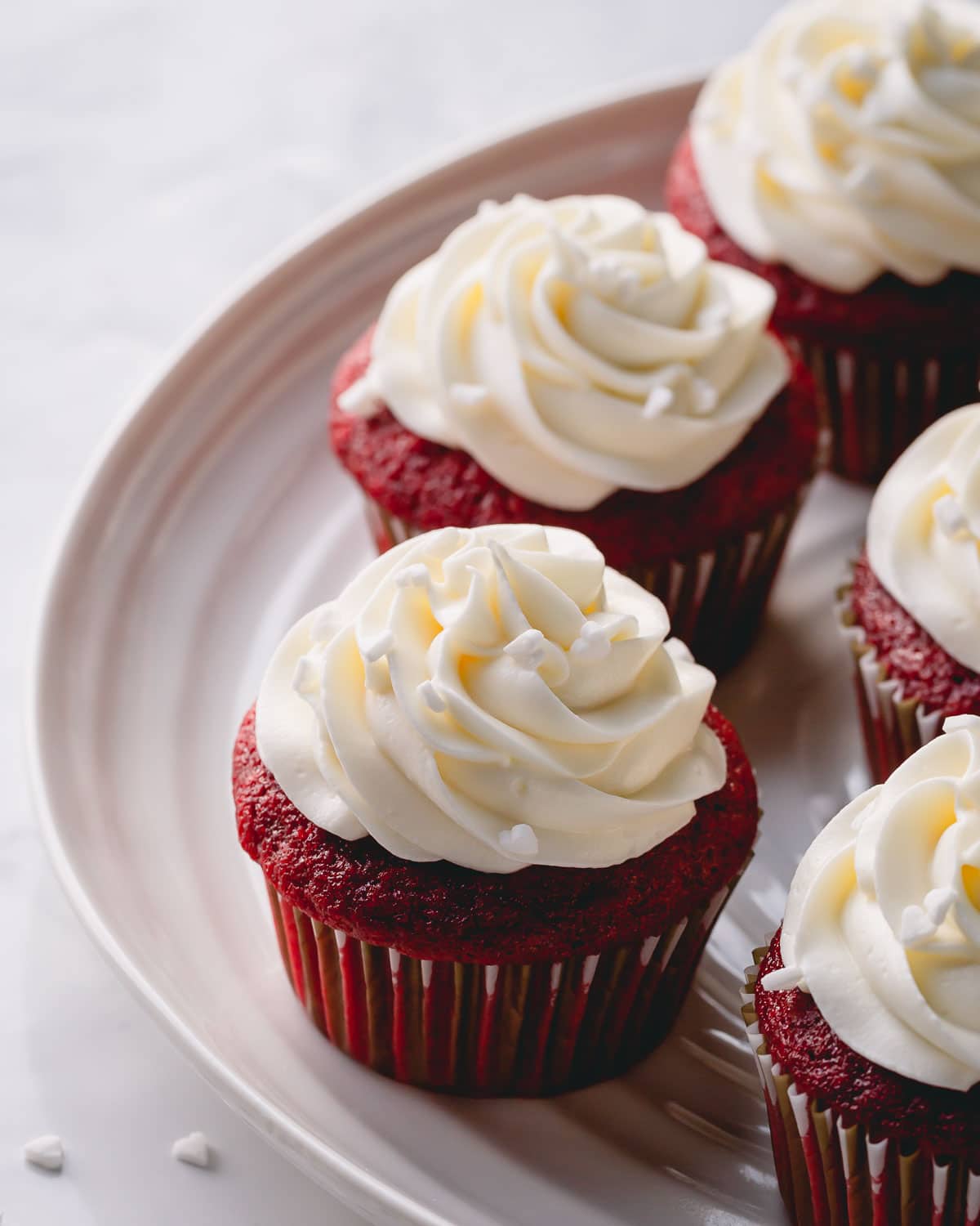 A platter of red velvet cupcakes with tall cream cheese frosting.