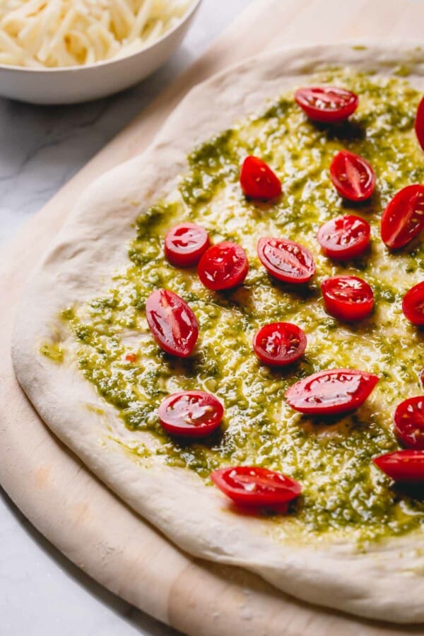 Unbaked pizza topped with pesto and sliced cherry tomatoes.