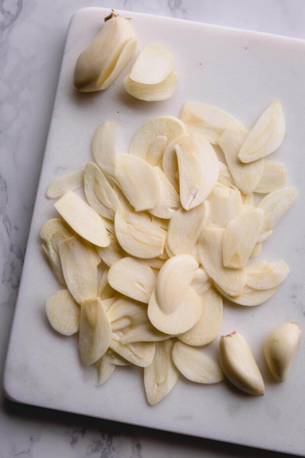 thinly sliced garlic cloves on a white marble cutting board.