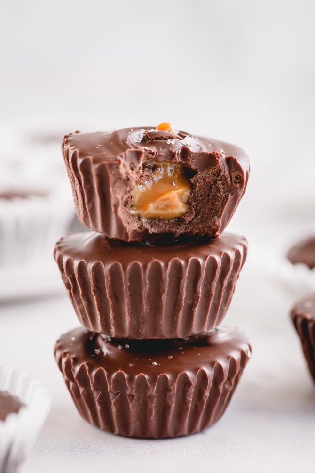 A bitten chocolate cup with exposed caramel filling stacked on top of 2 chocolate cups.