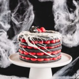 A 5-layer black macaron cake filled with red cream cheese filling on a white cake stand.
