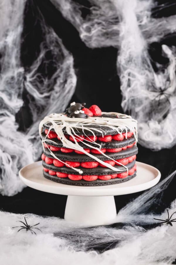 A 5-layer black macaron cake filled with red cream cheese filling on a white cake stand.
