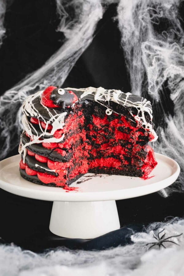5-layer black macaron cake filled with red cream cheese filling with a slice cut out.