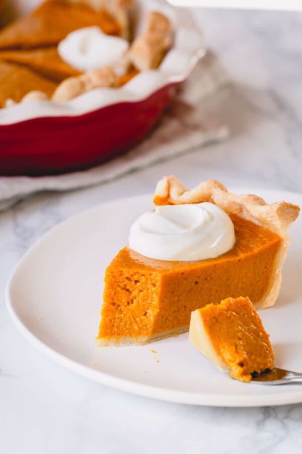 A slice of pumpkin pie with whipped cream and a small bite taken out.