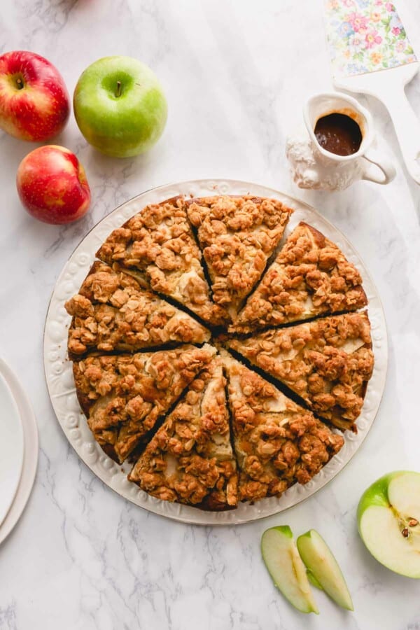 Overhead image of sliced apple coffee cake on a white serving plate.