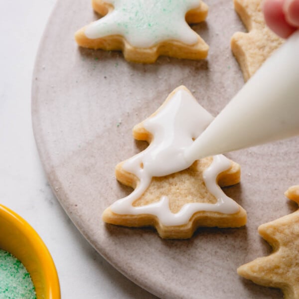 A christmas tree shaped sugar cookie being glazed with white powdered sugar icing.