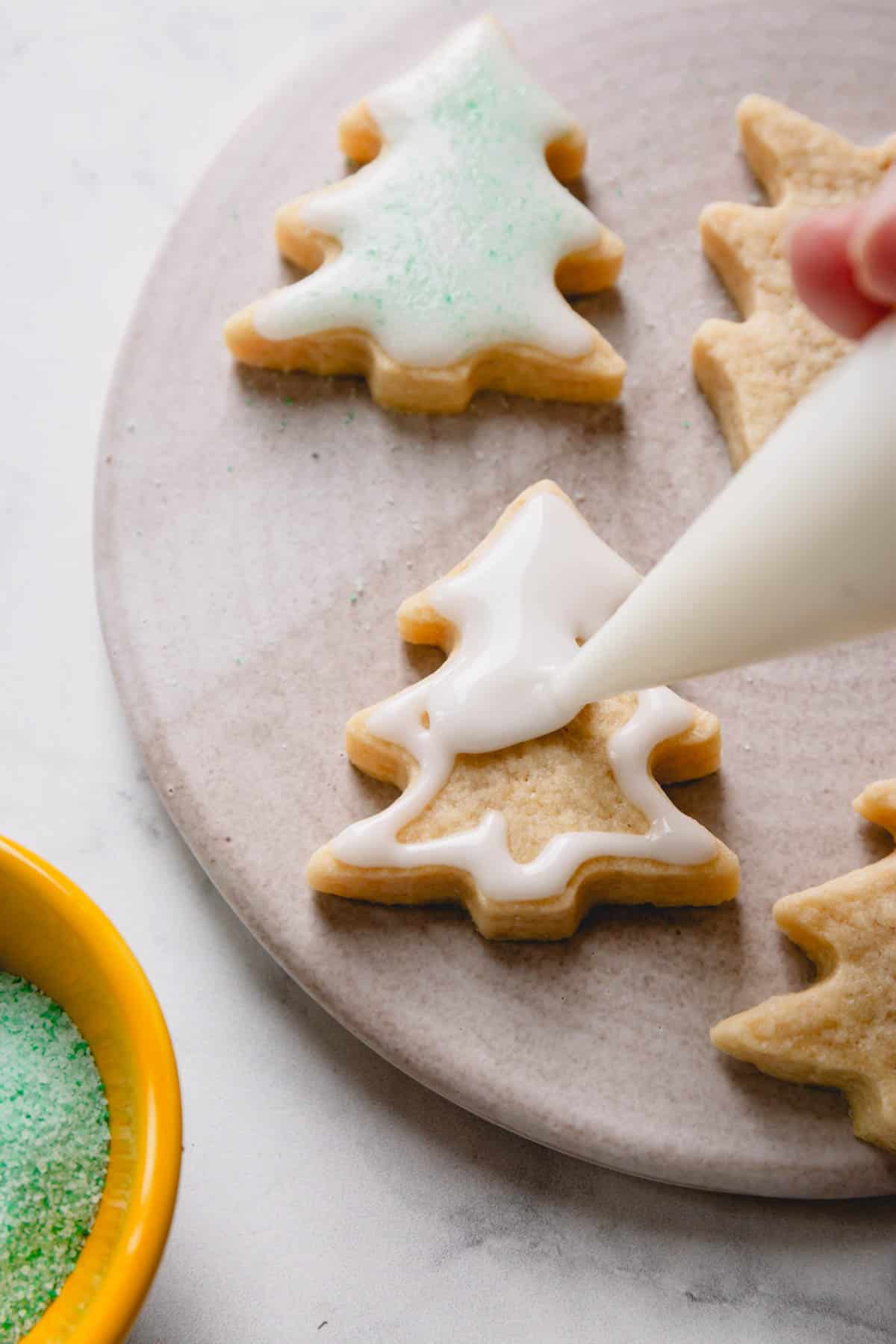 A christmas tree shaped sugar cookie being glazed with white powdered sugar icing.
