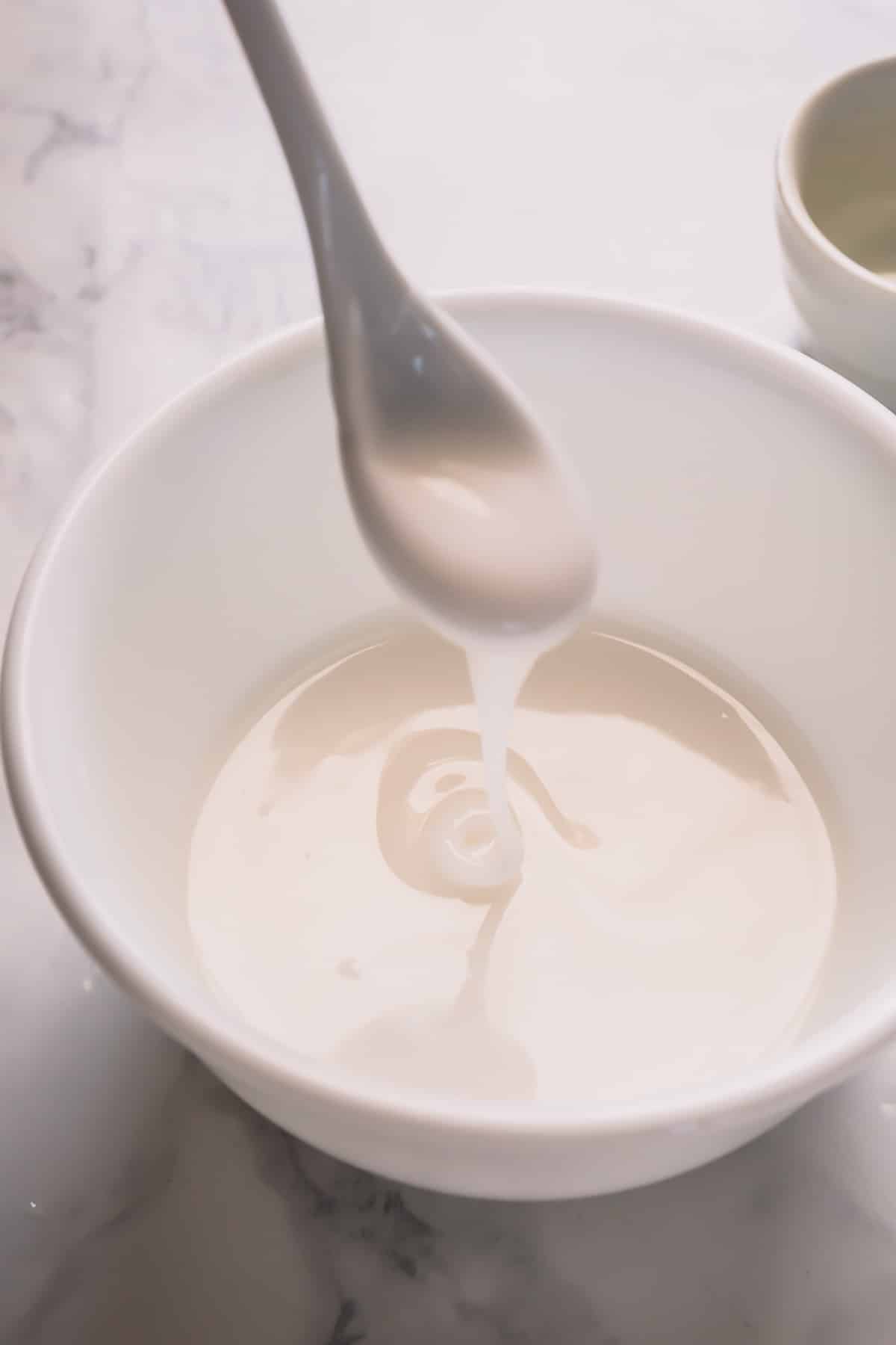 A white powdered sugar icing dripping from a spoon into a bowl of icing.