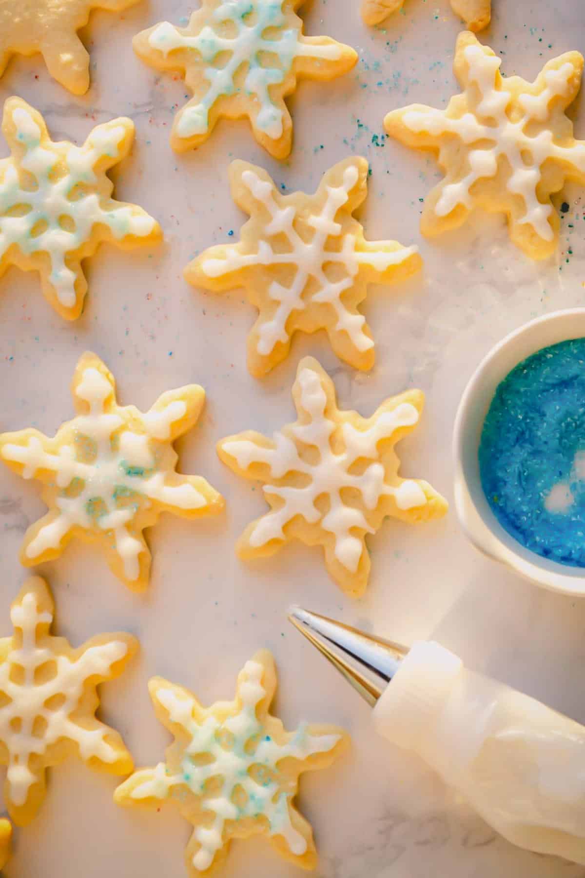 Snowflake shaped cookies decorated with powdered sugar glaze and blue icing sugar.