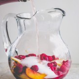 A glass pitcher filled with peach slices and raspberries and rose wine pouring in.