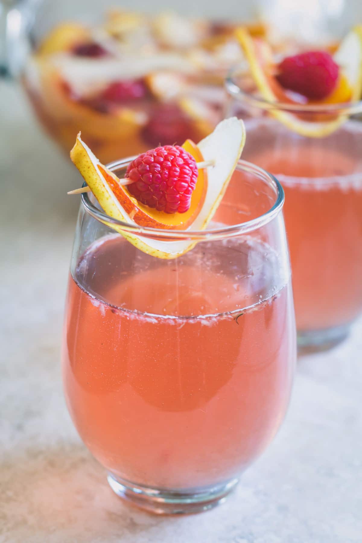 A glass of rose sangria garnished with slices of pear and peach and a raspberry.
