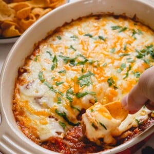 Bean dip in a casserole dish with a portion being scooped with a chip.