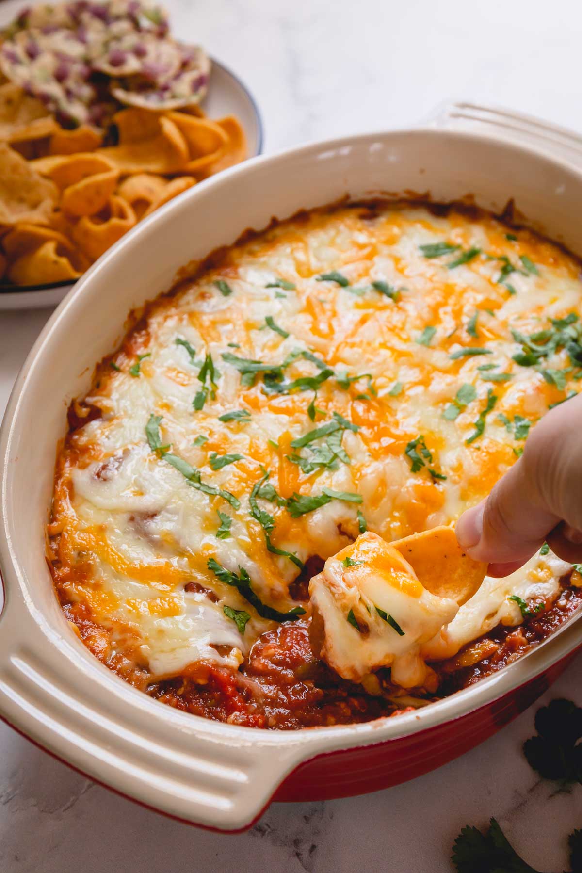 Bean dip in a casserole dish with a portion being scooped with a chip.