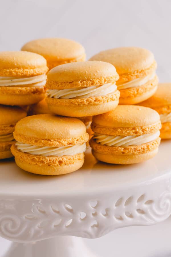 Bright yellow macarons stacked on a white cake platter.