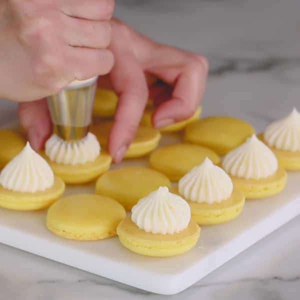 Piping a dollop of buttercream on macaron halves.