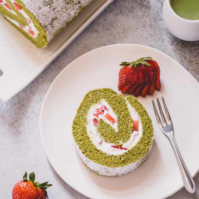 A slice of strawberry matcha roll cake on a white serving plate.