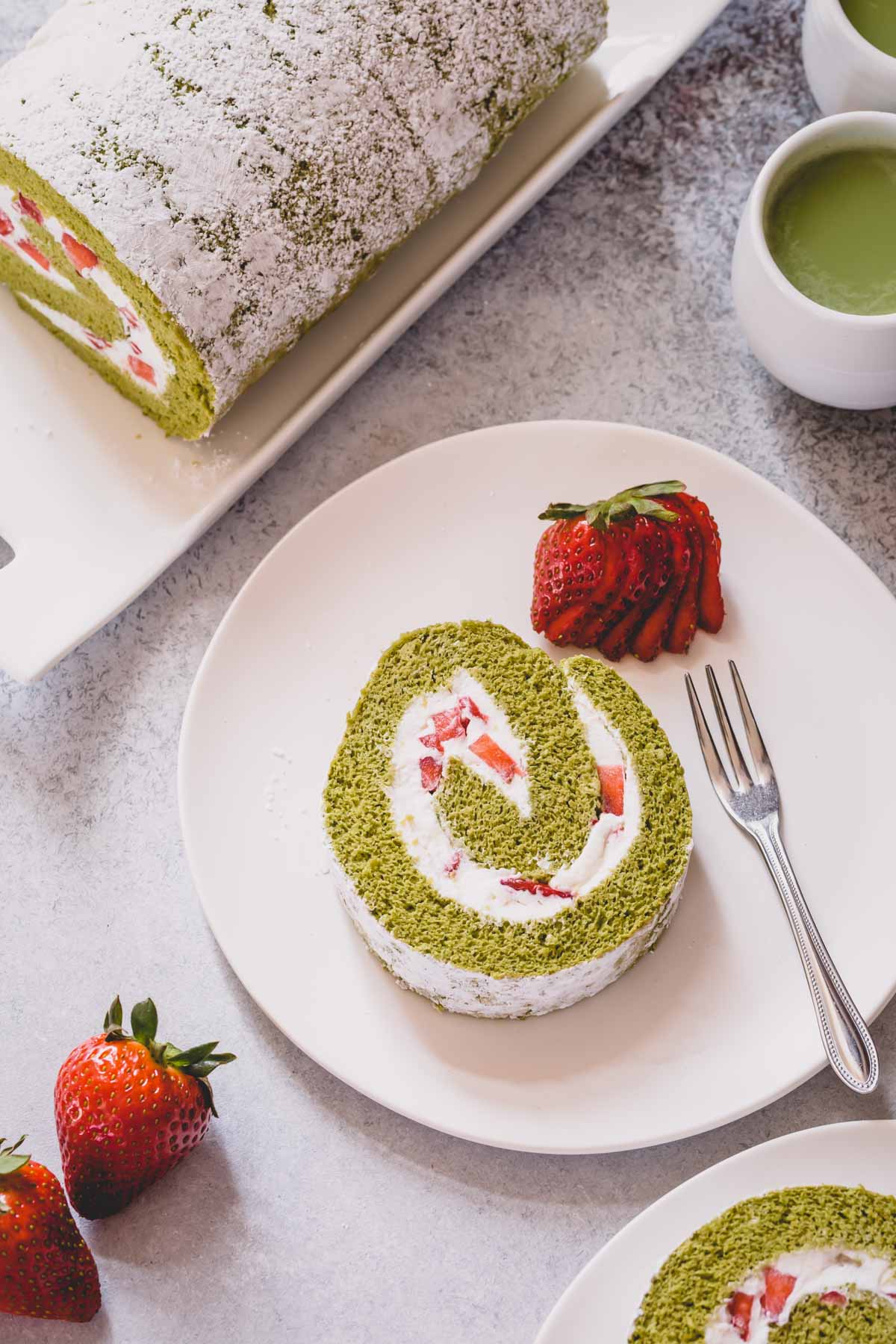 A slice of strawberry matcha roll cake on a white serving plate.