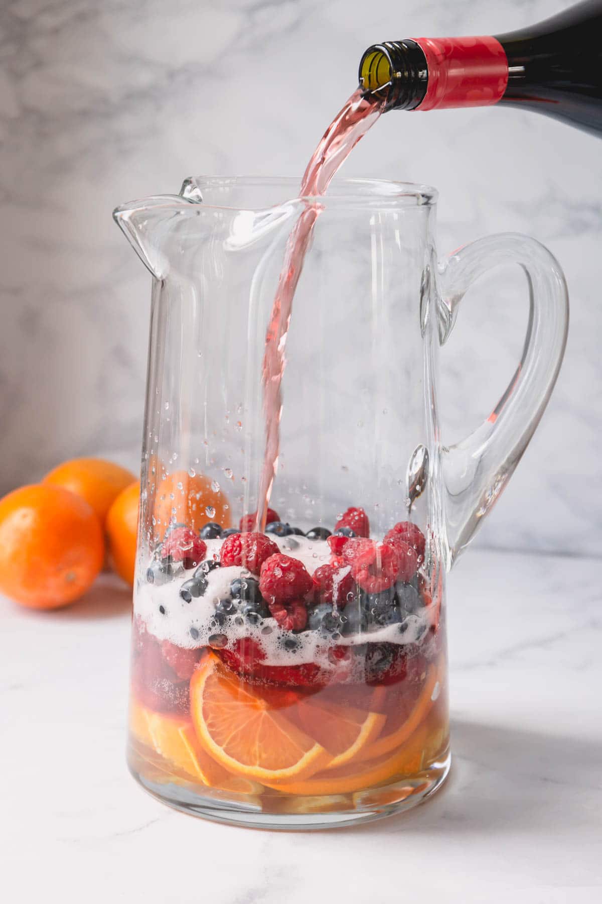A pitcher of sliced oranges and berries with pink Moscato is pouring into it.