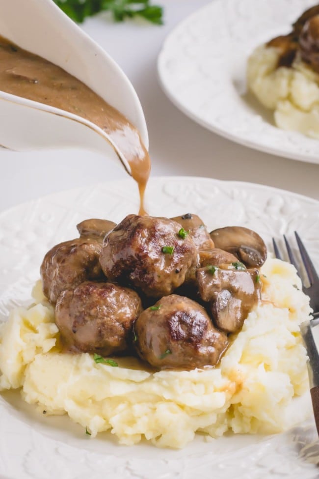 Brown gravy pouring over the meatballs and mashed potatoes on a white plate.