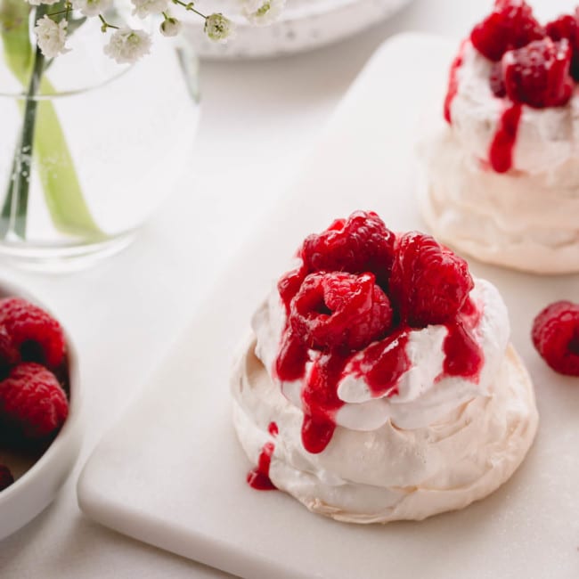 Mini pavlova topped with raspberry whipped cream, raspberry sauce and fresh raspberries.
