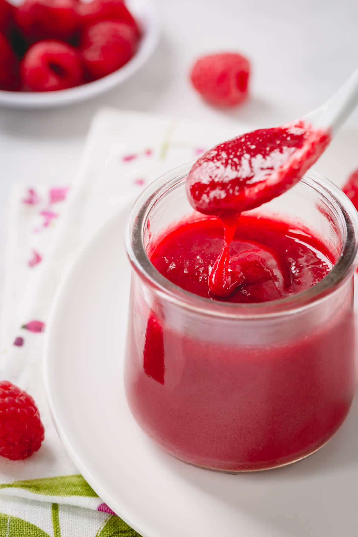 Raspberry coulis in a glass jar with a spoon of puree dripping down.