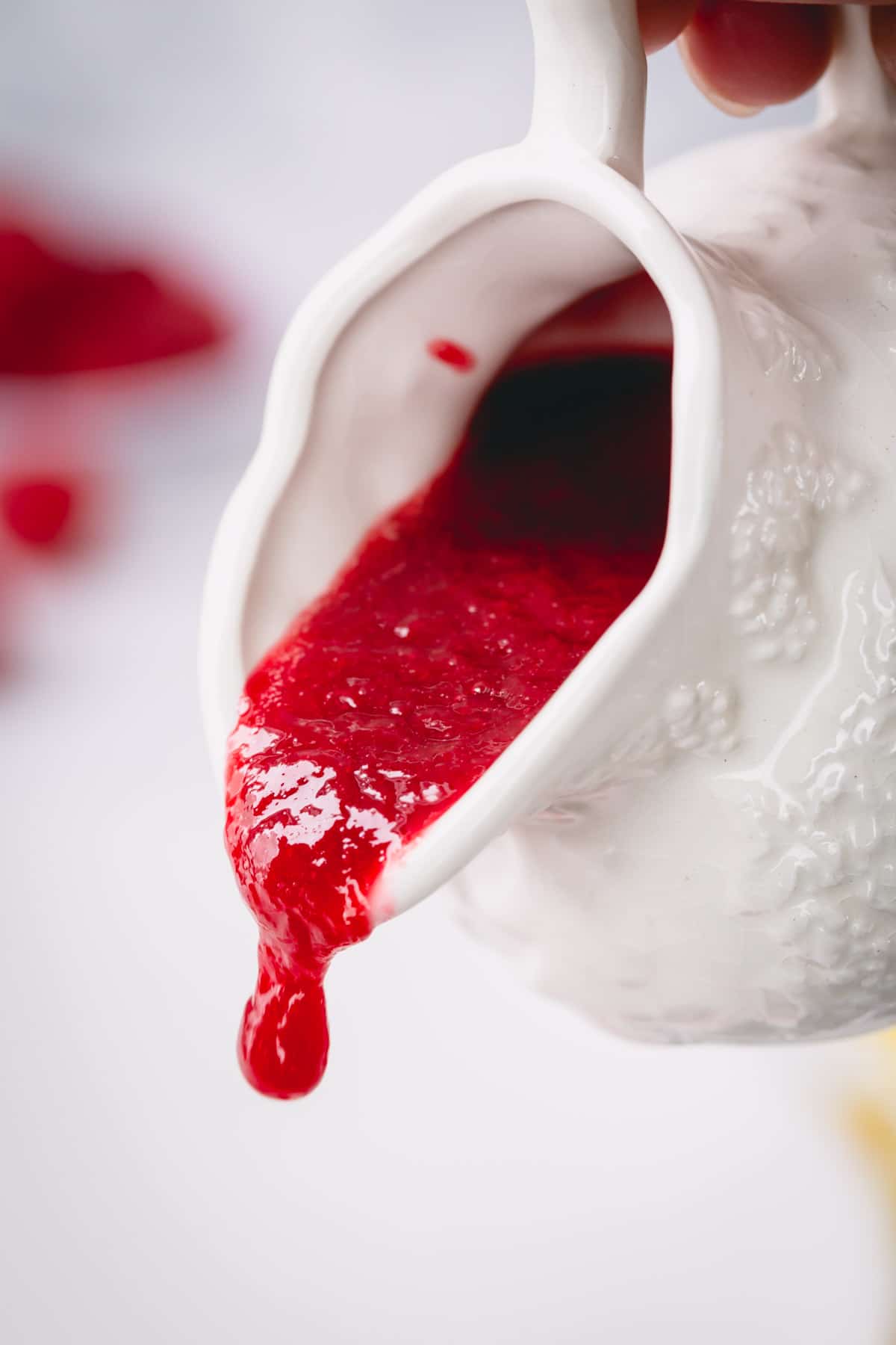 Raspberry sauce is being poured from a white sauce pitcher.
