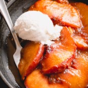 Caramelized peaches in a bowl topped with a scoop of vanilla ice cream.