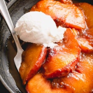 Caramelized peaches in a bowl topped with a scoop of vanilla ice cream.