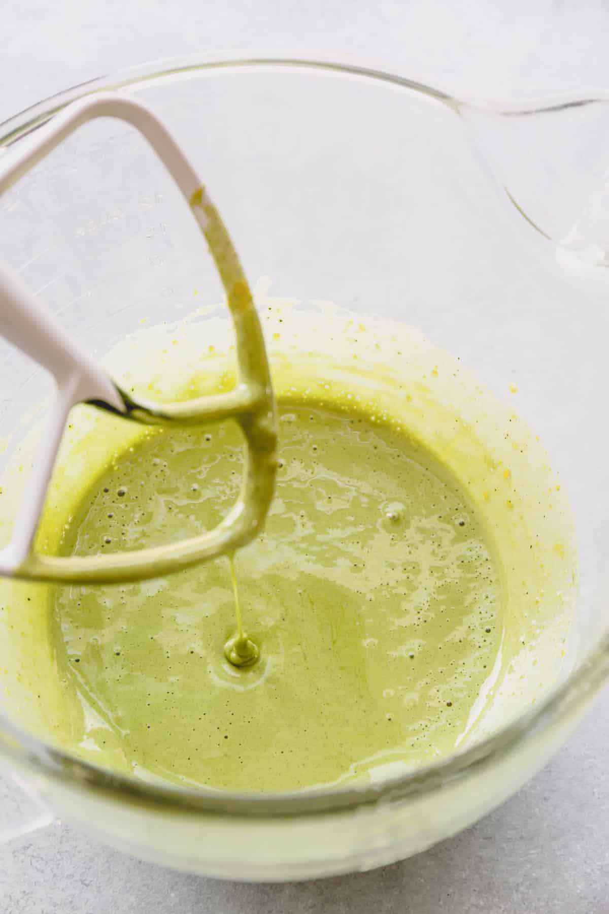 Pale green batter in a glass mixing bowl with paddle attachment.