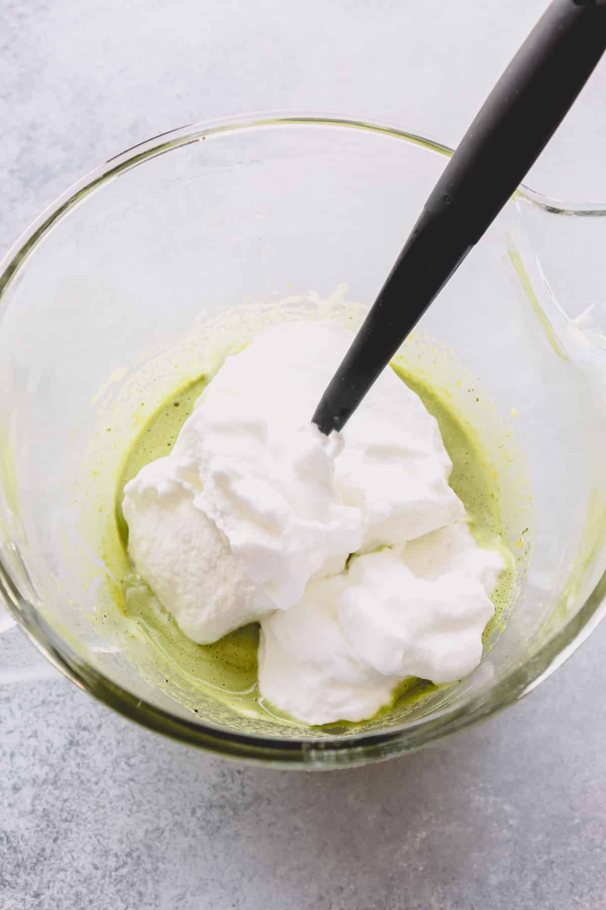 Whipped meringue added to the green batter in a mixing bowl.
